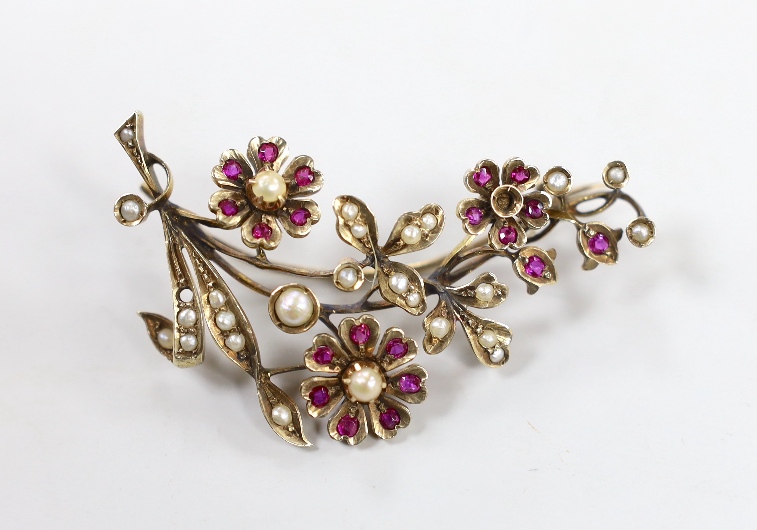 An early to mid 20th century, yellow metal, ruby and seed pearl cluster set floral spray brooch, 55mm, gross weight 13.3 grams (two pearls missing).